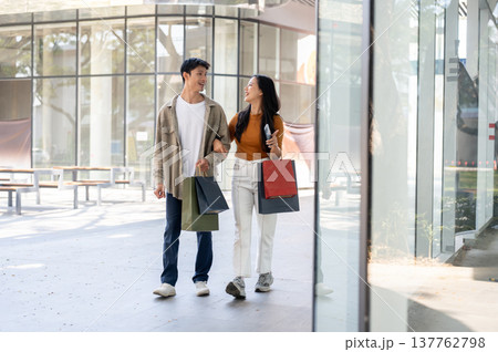 Full body of asian couple woman holding shopping bag pointing linking arms with man walking in mall. Full body of asian couple woman holding shopping bag pointing linking arms with man walking in mall. 137762798