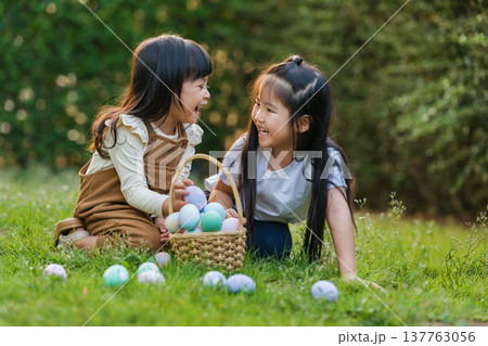 two happy child girl playing together and hunting for Easter eggs into basket on green grass in garden 137763056