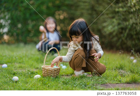two child girl playing together and hunting for Easter eggs into basket on green grass in garden two child girl playing together and hunting for Easter eggs into basket on green grass in garden 137763058
