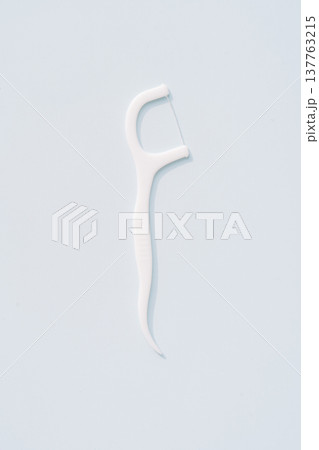Single white dental floss pick isolated on light blue background, minimal oral hygiene concept Single white dental floss pick isolated on light blue background, minimal oral hygiene concept 137763215