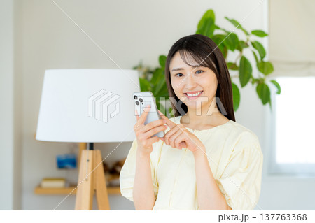部屋でスマホを操作する女性 137763368