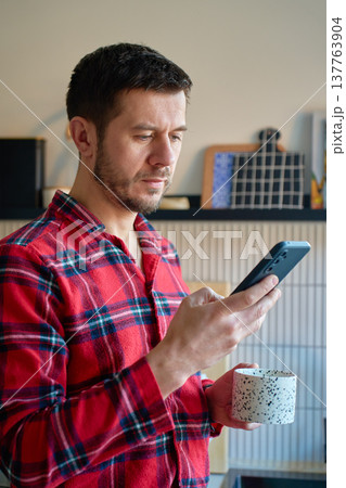 Man in pajamas drinking coffee and using smartphone at home 137763904