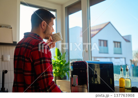 Man drinking coffee in kitchen by window at home in morning Man drinking coffee in kitchen by window at home in morning 137763908