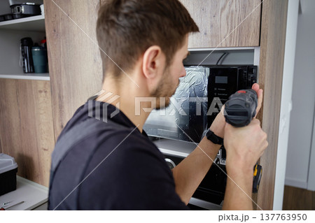 Man Using Power Drill to Fix Microwave Oven in Kitchen Cabinet Man Using Power Drill to Fix Microwave Oven in Kitchen Cabinet 137763950