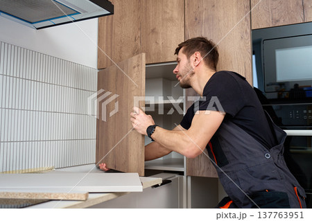 Handyman fitting a cabinet door panel in a modern kitchen 137763951