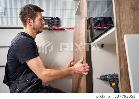 Handyman fitting kitchen cabinet panel during installation Handyman fitting kitchen cabinet panel during installation 137763953