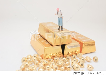 Miniature explorer stands proudly atop stacked shining gold bars 137764749