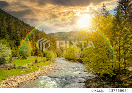 sunset over river in mountain landscape. wonderful springtime countryside scenery. blue green water among forest and rocky shore. wooden fence on the river bank. cloudy sky and rainbow sunset over river in mountain landscape. wonderful springtime countryside scenery. blue green water among forest and rocky shore. wooden fence on the river bank. cloudy sky and rainbow 137766684