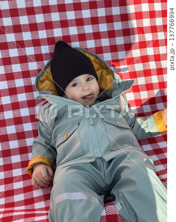 Smiling toddler in winter snowsuit on red checkered blanket Smiling toddler in winter snowsuit on red checkered blanket 137766994