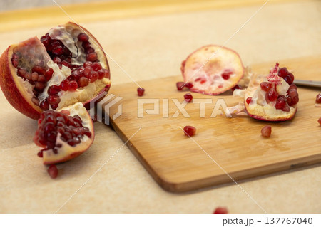 Cut pomegranate on cutting board with scattered arils 137767040