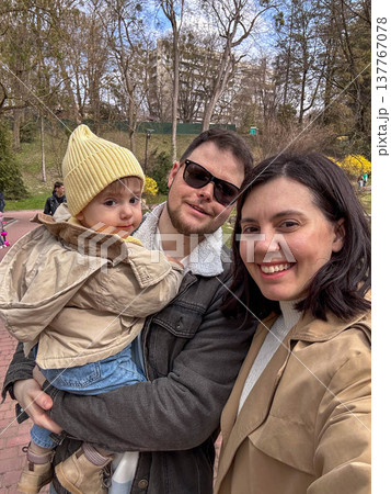 Happy family selfie in park with toddler wearing yellow beanie 137767078