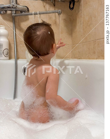 Toddler in bubble bath reaching for shower hose Toddler in bubble bath reaching for shower hose 137767163