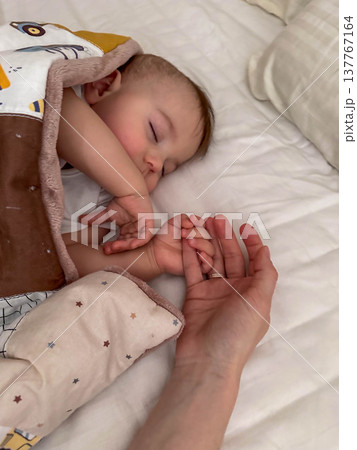 Peaceful sleeping baby holding adult hand Peaceful sleeping baby holding adult hand 137767164