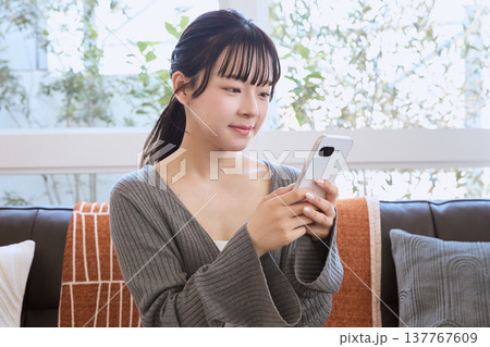 リビングでスマートフォンを見る女性　リビングでくつろぐライフスタイル 137767609