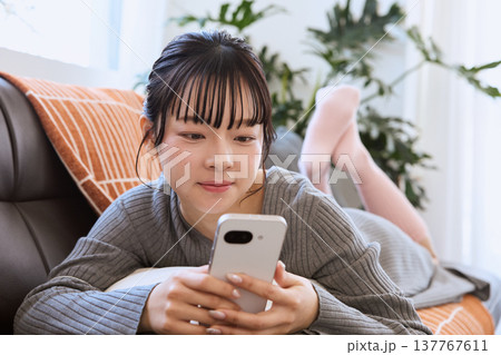 ヘッドホンでスマートフォンを楽しむ女性　リビングでくつろぐライフスタイル 137767611