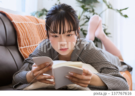 ソファで寝転び本を読む女性　自宅でくつろぐ読書の時間 137767616