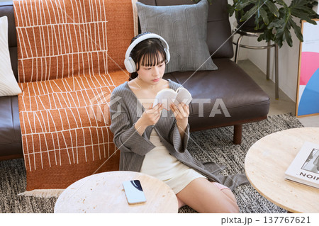 ヘッドホンで音楽を聴きながら本を読む女性　自宅で過ごすリラックスタイム 137767621