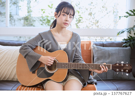 自宅のリビングでアコースティックギターを弾く若い女性 自宅のリビングでアコースティックギターを弾く若い女性 137767627