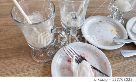 Empty coffee glasses with foam traces and dirty plates on a wooden cafe table after a finished meal 137768022