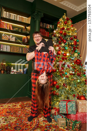 Family member lifts child for fun in living room by Christmas tree Family member lifts child for fun in living room by Christmas tree 137768504