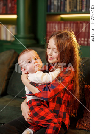 Little girl holds baby brother in cozy room with books 137768505