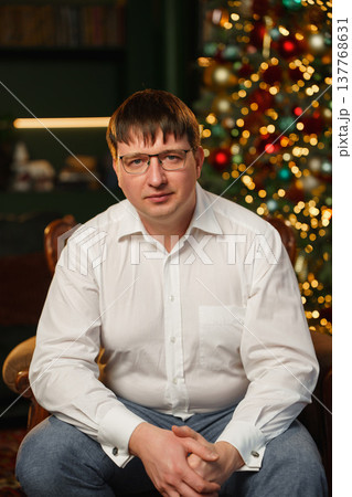 Man sitting in front of a Christmas tree with lights at home Man sitting in front of a Christmas tree with lights at home 137768631
