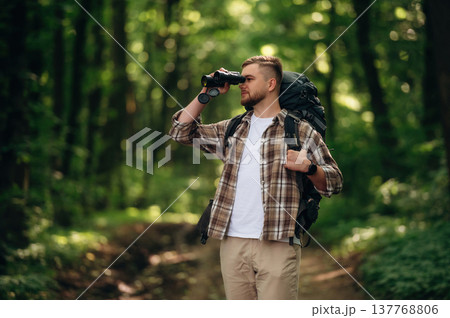 Using binoculars. Male tourist is with backpack in the forest Using binoculars. Male tourist is with backpack in the forest 137768806