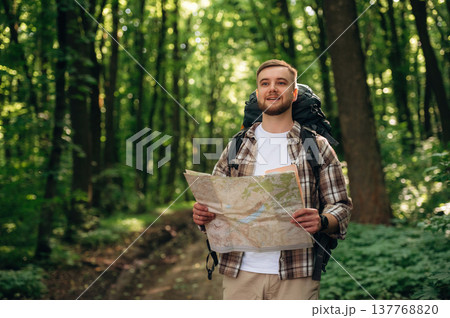 Searching the way, holding map. Male tourist is with backpack in the forest Searching the way, holding map. Male tourist is with backpack in the forest 137768820