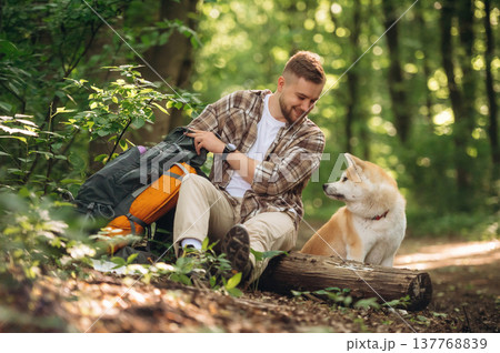 Tranquil, resting by sitting on the log. Man tourist is with his dog in the forest 137768839