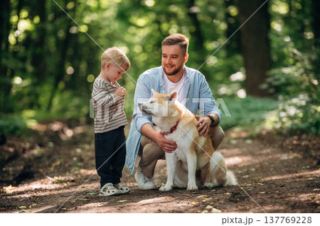 Sitting, playing with pet. Father with son and dog are in the forest Sitting, playing with pet. Father with son and dog are in the forest 137769228