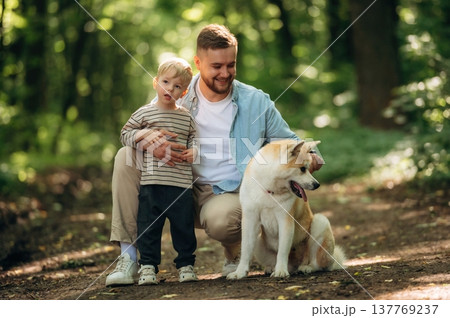 Positive facial expression, sitting. Father with son and dog are in the forest Positive facial expression, sitting. Father with son and dog are in the forest 137769237