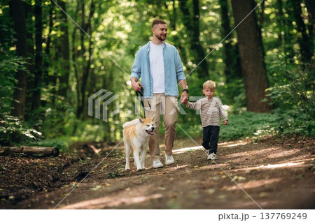 Free time, having a walk, wellness. Father with son and dog are in the forest Free time, having a walk, wellness. Father with son and dog are in the forest 137769249