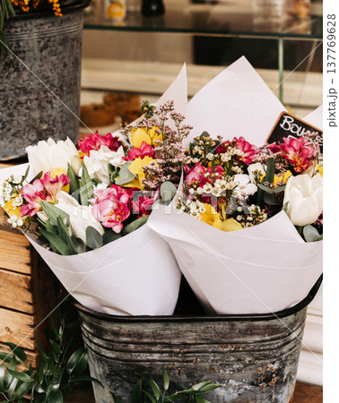 Colorful spring flower bouquets wrapped in paper and placed in a rustic metal bucket at a market stall Colorful spring flower bouquets wrapped in paper and placed in a rustic metal bucket at a market stall 137769628