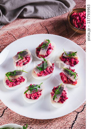 Eggs delived with vegetable salad, a piece of herring and arugula on a plate on the table vertical view Eggs delived with vegetable salad, a piece of herring and arugula on a plate on the table vertical view 137769963