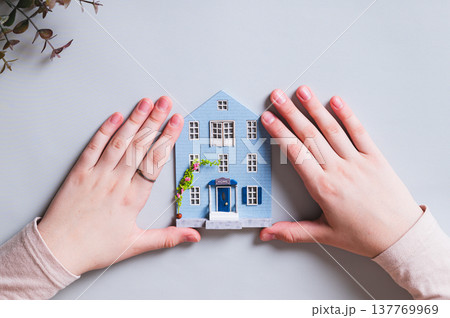 House figurine and children's hands on a blue background, concept of comfort House figurine and children's hands on a blue background, concept of comfort 137769969