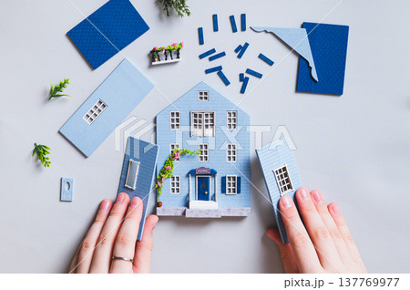 A girl assembles a miniature toy house from parts on a blue background top view A girl assembles a miniature toy house from parts on a blue background top view 137769977