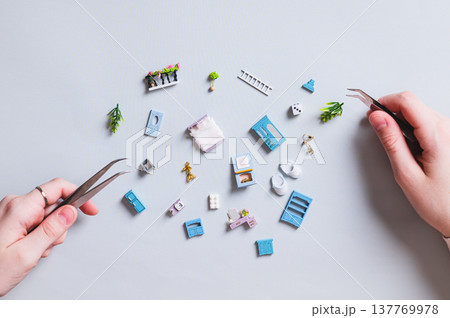 Miniature toy house parts and children's hands with tweezers on a blue background 137769978