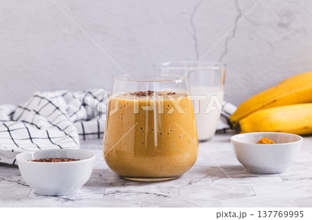 Smoothie made from coconut milk, banana, turmeric and flax seeds in a glass on the table 137769995