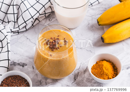 Mix of banana, turmeric and plant milk in a glass on a table 137769996