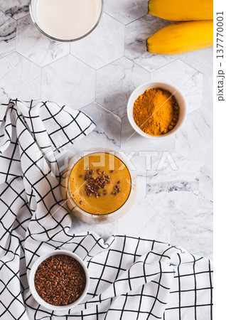 Mix of banana, turmeric and plant milk in a glass on a table top and vertical view Mix of banana, turmeric and plant milk in a glass on a table top and vertical view 137770001