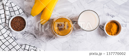 Mix of banana, turmeric and plant milk in a glass on a table top view web banner Mix of banana, turmeric and plant milk in a glass on a table top view web banner 137770002