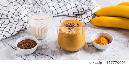 Smoothie made from coconut milk, banana, turmeric and flax seeds in a glass web banner Smoothie made from coconut milk, banana, turmeric and flax seeds in a glass web banner 137770003
