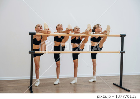 Stretching the legs. Girls practicing ballet indoors in the class Stretching the legs. Girls practicing ballet indoors in the class 137770115