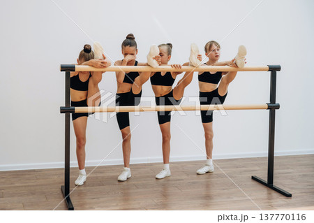 Stretching the legs. Girls practicing ballet indoors in the class Stretching the legs. Girls practicing ballet indoors in the class 137770116