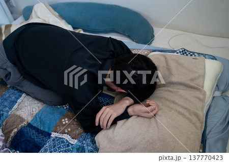 布団で顔を枕に埋めて寝る男性 137770423