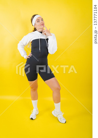 Young woman thinking in sporty outfit on yellow background Young woman thinking in sporty outfit on yellow background 137771184
