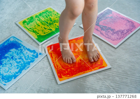Child feet standing on colorful sensory gel mat on floor during tactile play activity. Sensory stimulation, autism support and occupational therapy development concept. 137771268