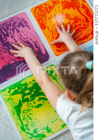 Little girl pressing colorful sensory gel mats with both hands during tactile play activity at home. Sensory integration, autism support and occupational therapy development concept. 137771271