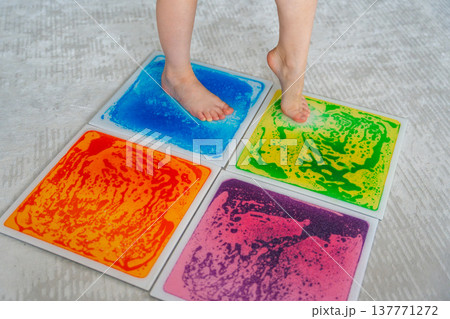 Child feet standing on colorful sensory gel mat on floor during tactile play activity. Sensory stimulation, autism support and occupational therapy development concept. 137771272