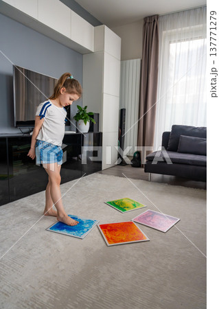 Little girl stepping and jumping on colorful sensory gel mats placed on floor at home. Sensory development, autism support and occupational therapy activity concept. 137771279